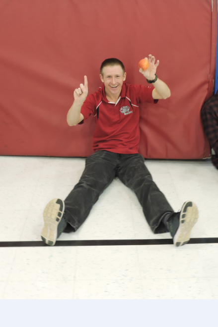 A student sits on the ground and smiles with an apple.